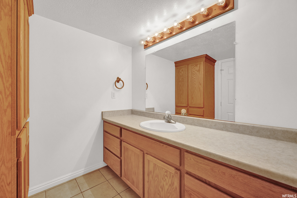 Bathroom with mirror, vanity, light tile flooring, and a textured ceiling