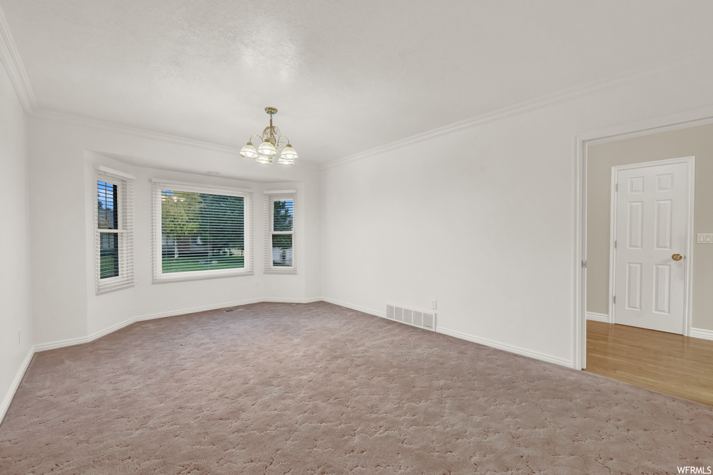 Unfurnished room featuring an inviting chandelier, light colored carpet, and ornamental molding