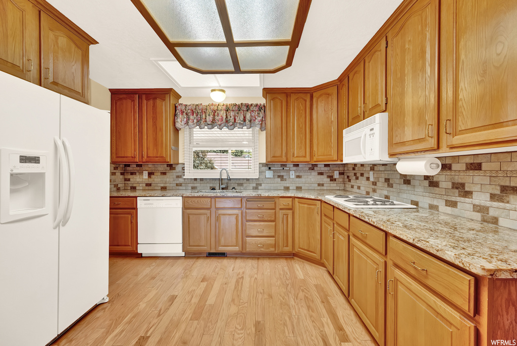 Kitchen featuring light hardwood flooring, backsplash, brown cabinets, white appliances, and light countertops