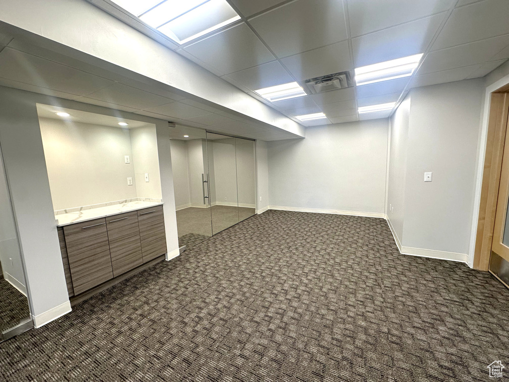 Basement featuring a drop ceiling and dark colored carpet