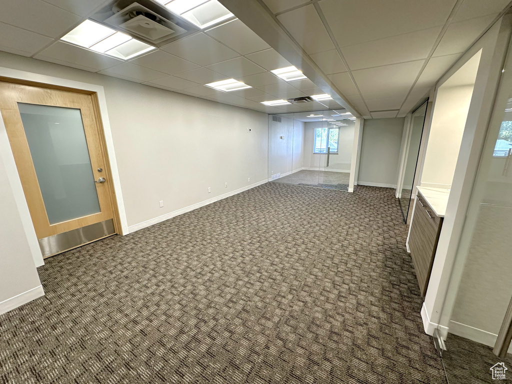 Basement featuring dark carpet and a paneled ceiling