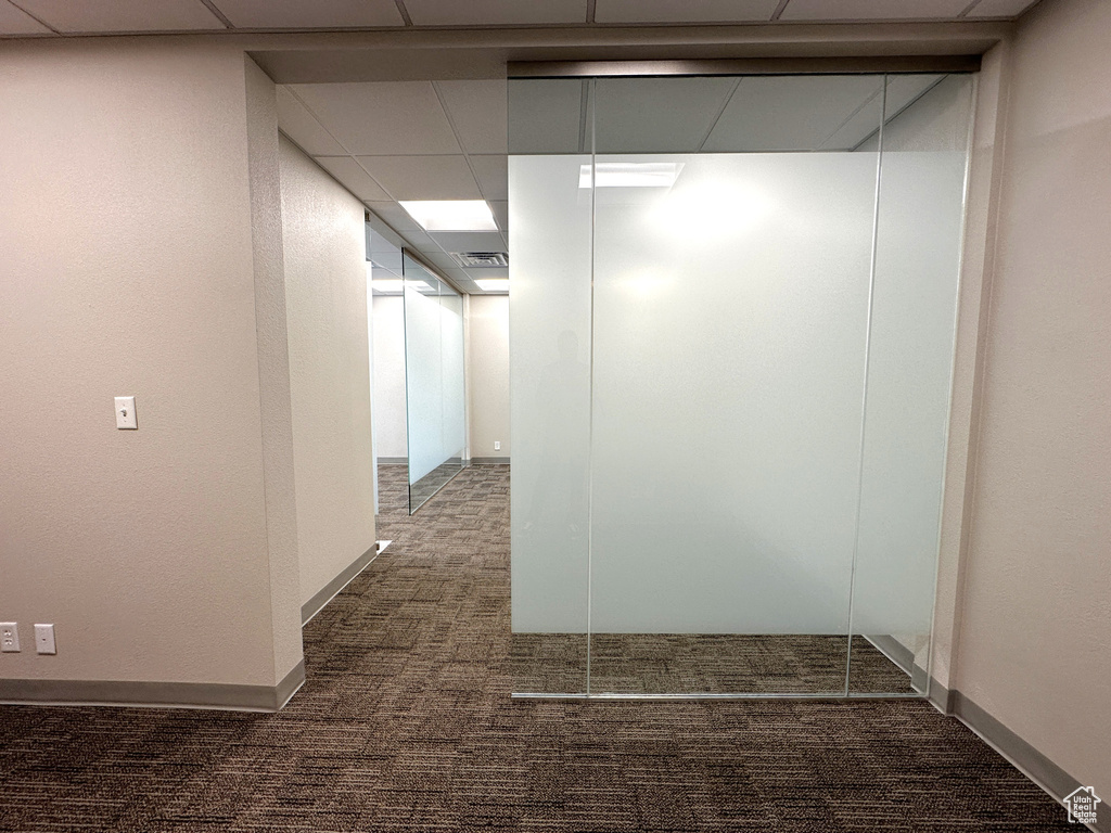 Hall featuring a paneled ceiling and dark colored carpet