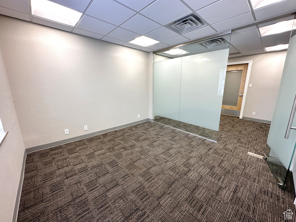 Empty room with a drop ceiling and dark colored carpet