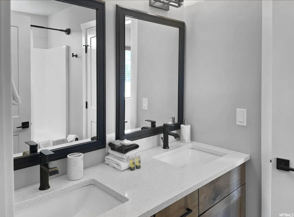 Bathroom featuring mirror, dual vanity, and shower / washtub combination