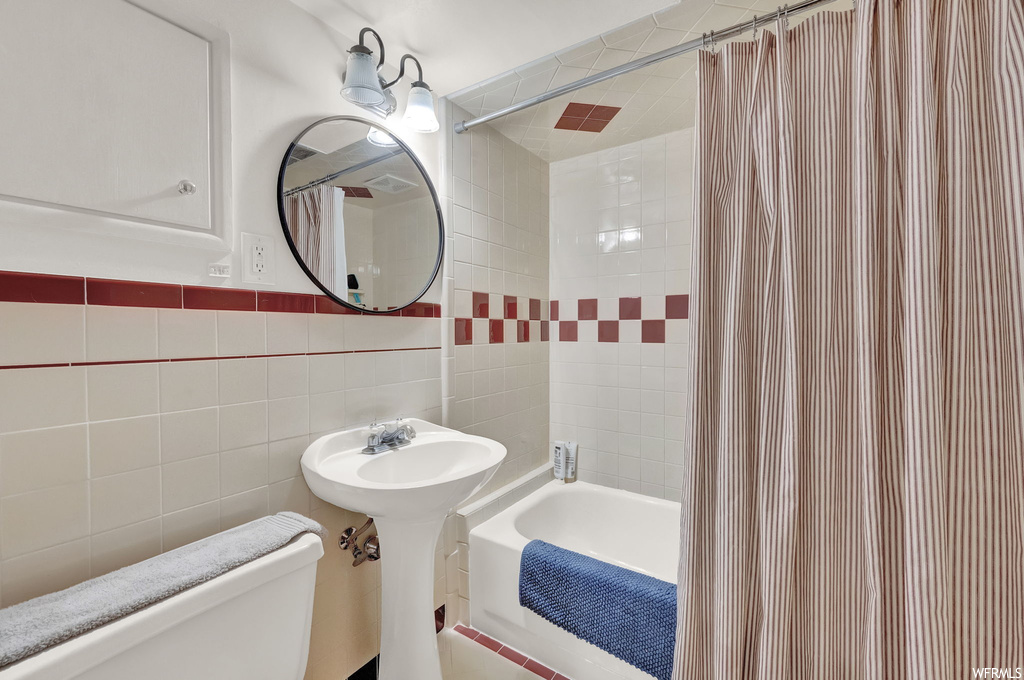 Full bathroom with shower / bath combo, tile walls, sink, backsplash, and mirror
