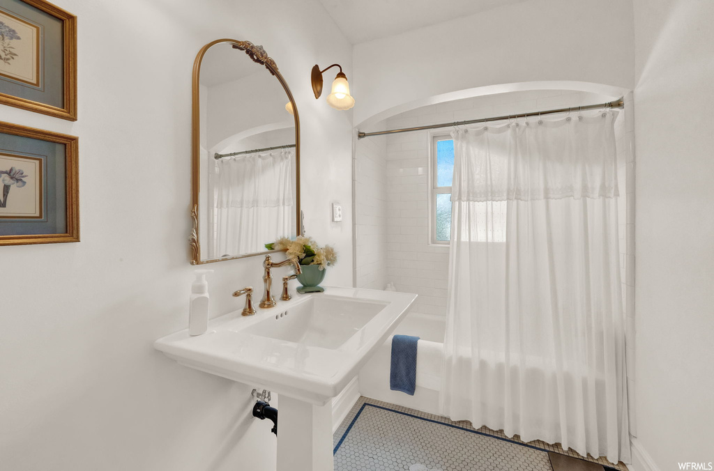 Bathroom featuring mirror, washbasin, shower / bath combination with curtain, and light tile flooring