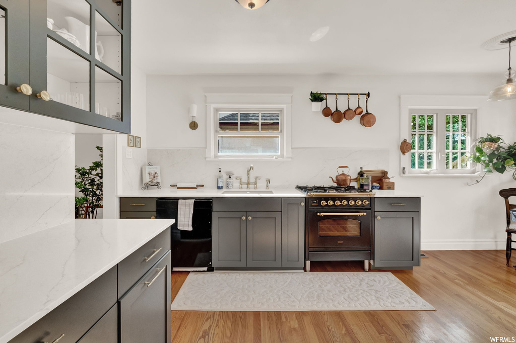 Kitchen featuring light parquet floors, dark brown cabinetry, light countertops, backsplash, dishwashing machine, and gas range