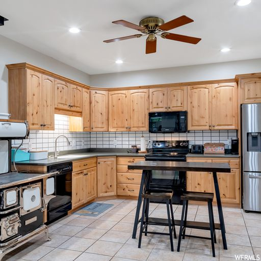 Kitchen with light tile floors, backsplash, ceiling fan, dark countertops, and black appliances