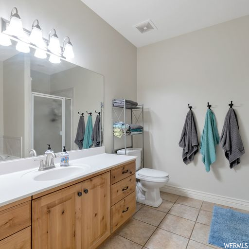 Bathroom featuring mirror, vanity, a shower with door, and light tile floors