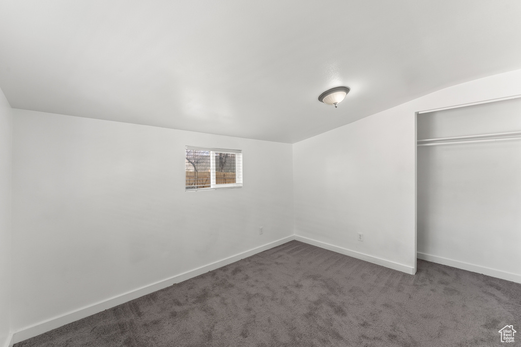 Unfurnished bedroom featuring a closet, dark carpet, and vaulted ceiling