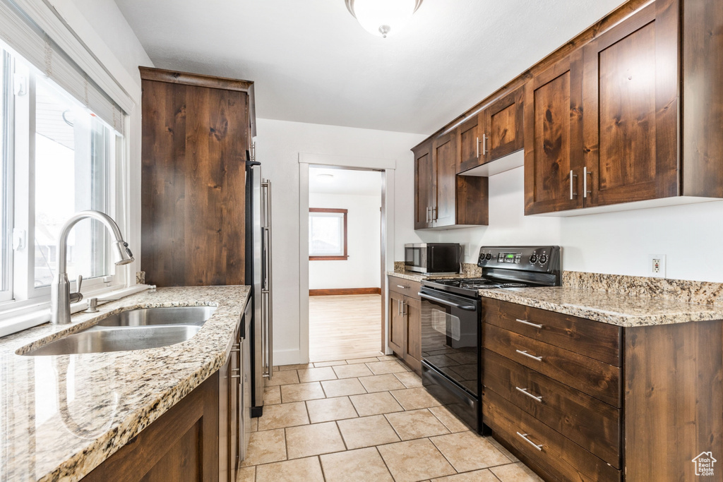 Kitchen featuring light tile flooring, sink, appliances with stainless steel finishes, and light stone counters
