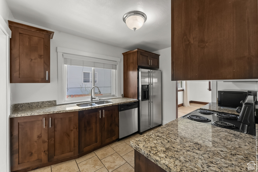 Kitchen featuring light stone countertops, sink, appliances with stainless steel finishes, dark brown cabinetry, and light tile floors