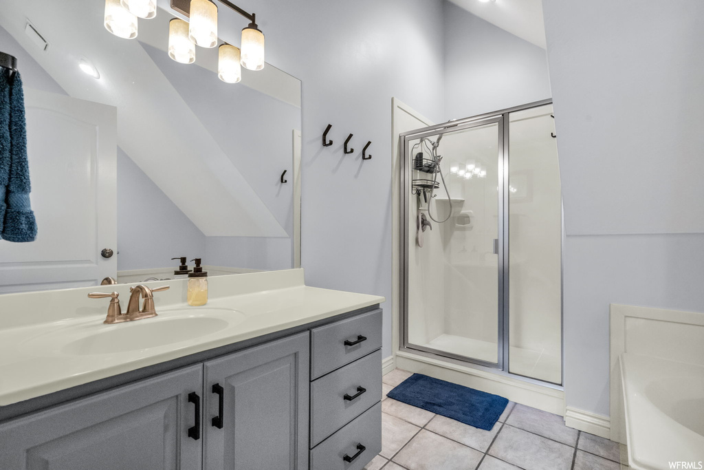 Bathroom with light tile flooring, vanity with extensive cabinet space, lofted ceiling, mirror, and separate shower and tub
