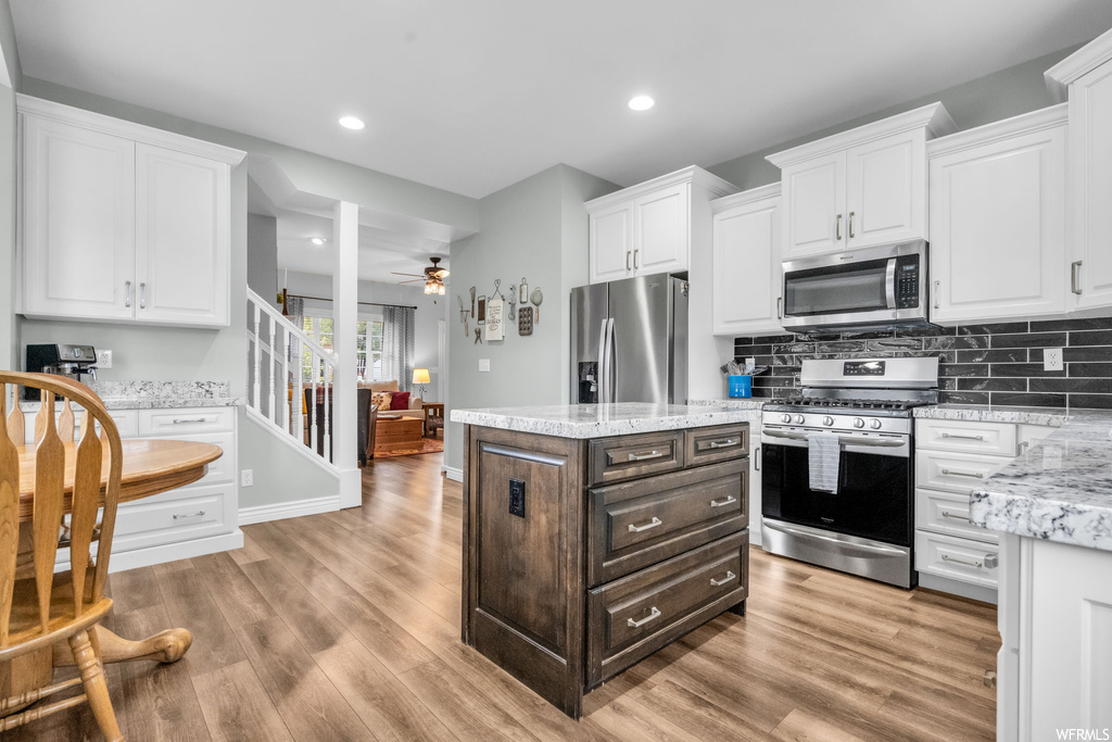 Kitchen with light stone counters, backsplash, ceiling fan, light hardwood floors, appliances with stainless steel finishes, and white cabinetry