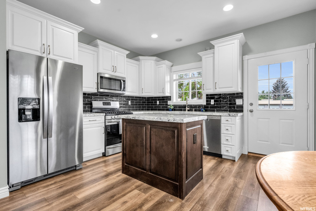 Kitchen with backsplash, light hardwood flooring, white cabinets, appliances with stainless steel finishes, and light stone countertops
