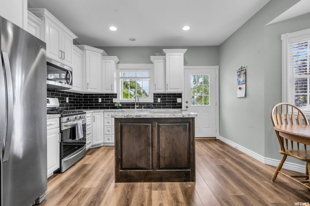 Kitchen featuring light parquet floors, stone countertops, white cabinets, backsplash, and appliances with stainless steel finishes