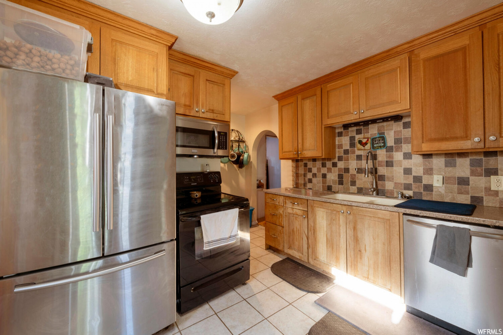 Kitchen featuring light tile floors, stainless steel appliances, backsplash, brown cabinets, and light countertops
