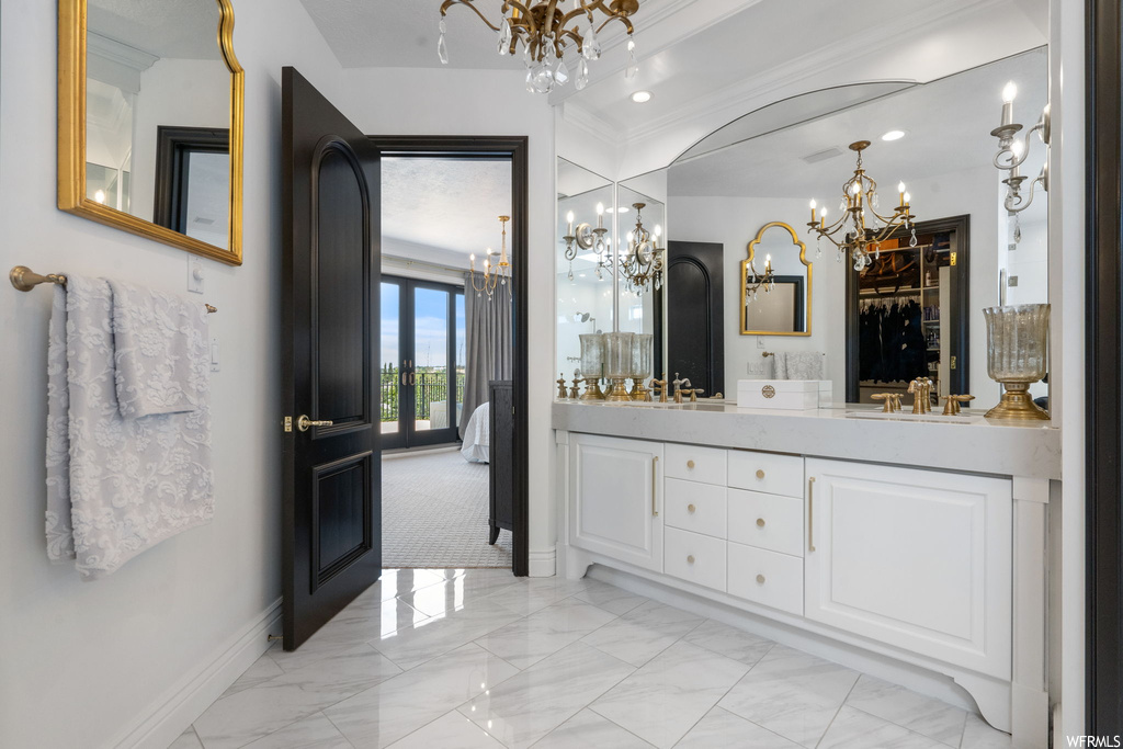 Bathroom featuring light tile floors, a chandelier, mirror, double large sink vanity, and crown molding
