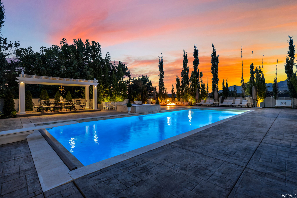 Pool at dusk featuring a pergola and a patio area