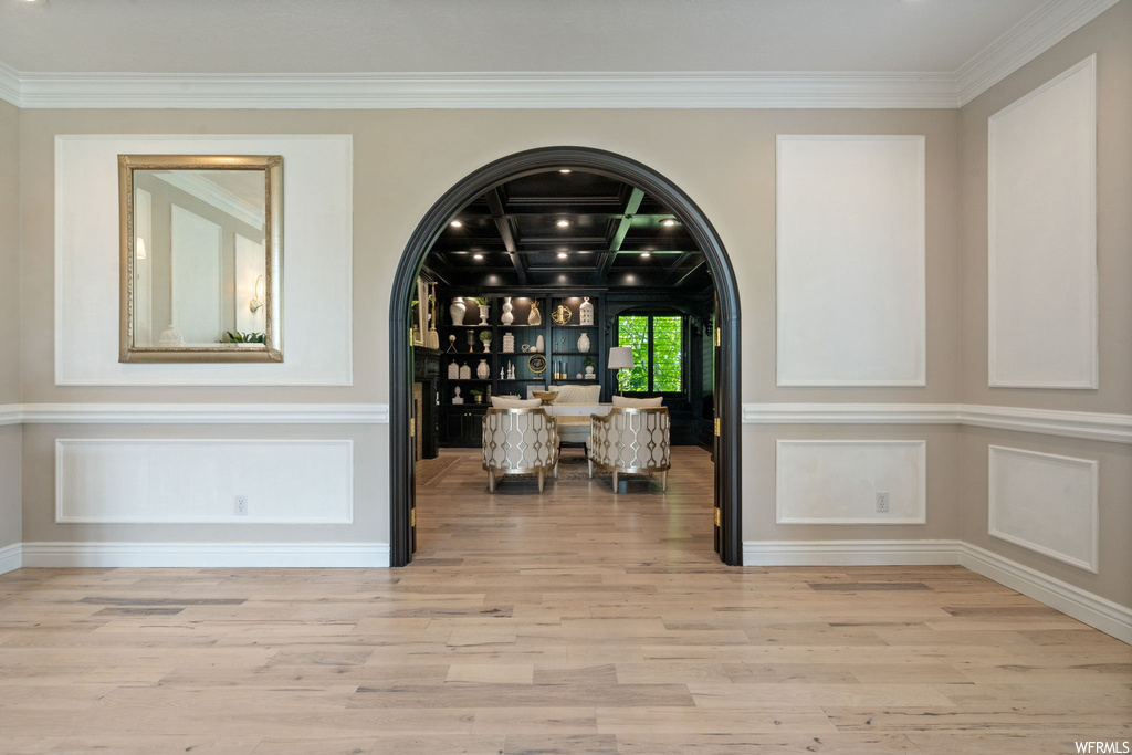 Interior space with coffered ceiling, light hardwood floors, ornamental molding, and beam ceiling