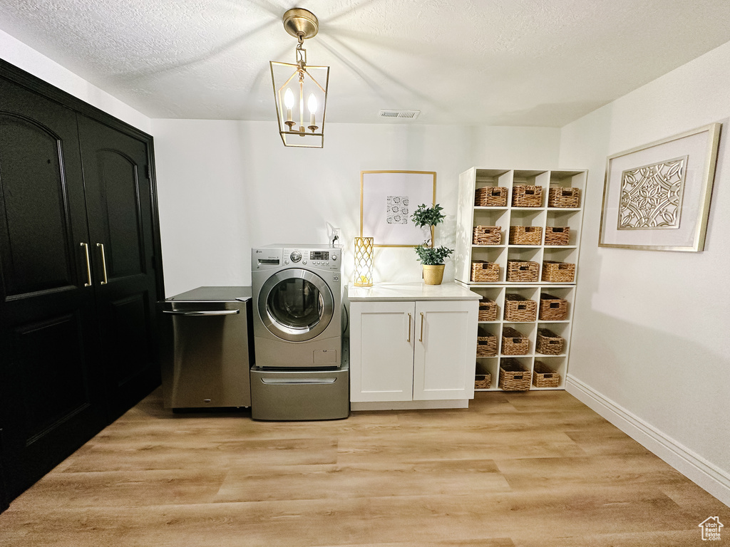 Clothes washing area with cabinets, light hardwood / wood-style floors, washer / dryer, and a notable chandelier