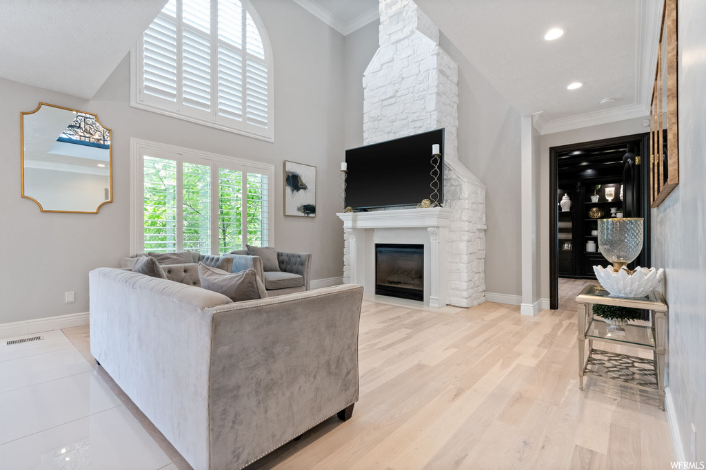Hardwood floored living room with a high ceiling, crown molding, and a fireplace