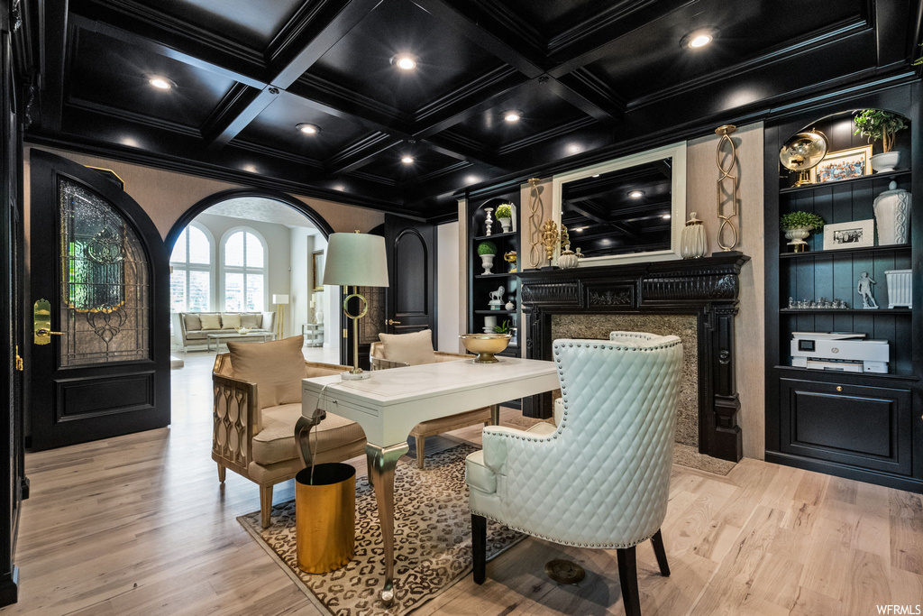 Wood floored dining area featuring built in features, beam ceiling, ornamental molding, coffered ceiling, and a fireplace
