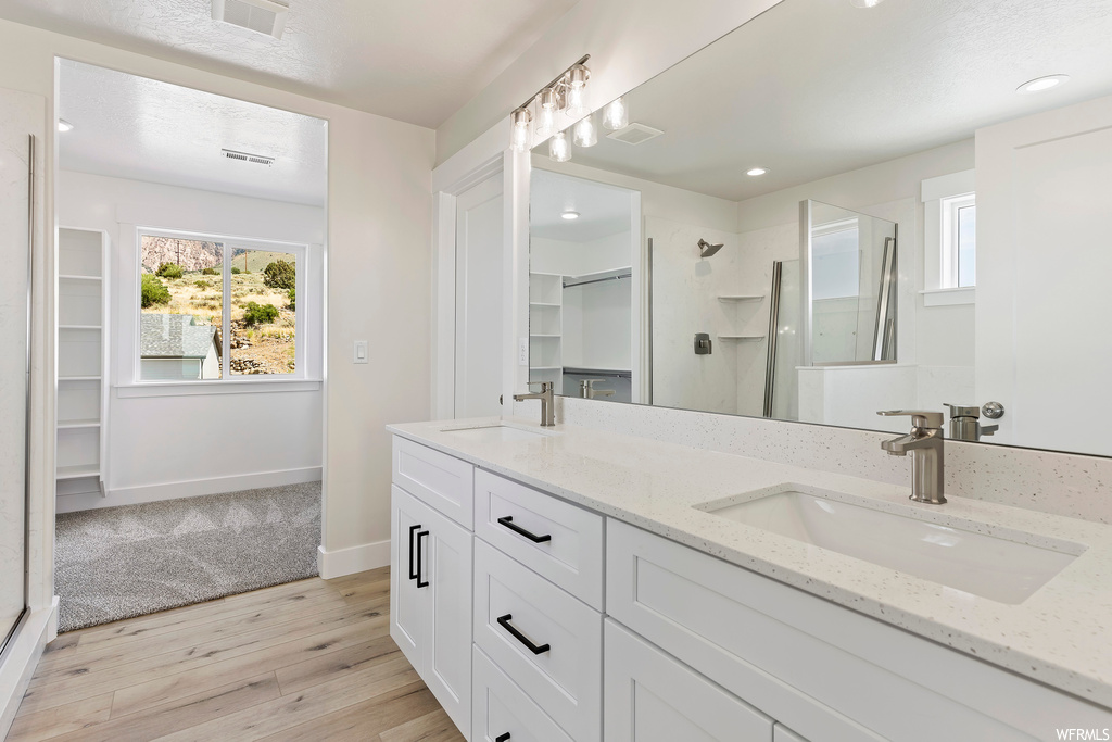 Bathroom with mirror, a shower with shower door, light hardwood floors, and dual large vanity