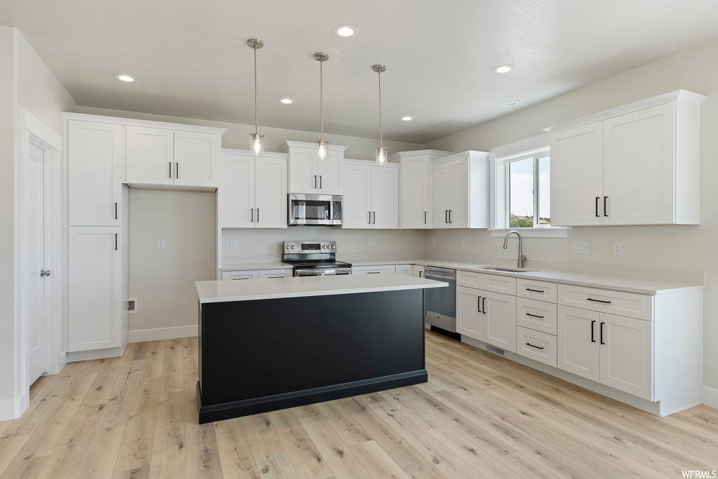Kitchen with hanging light fixtures, light hardwood floors, appliances with stainless steel finishes, light countertops, and white cabinetry