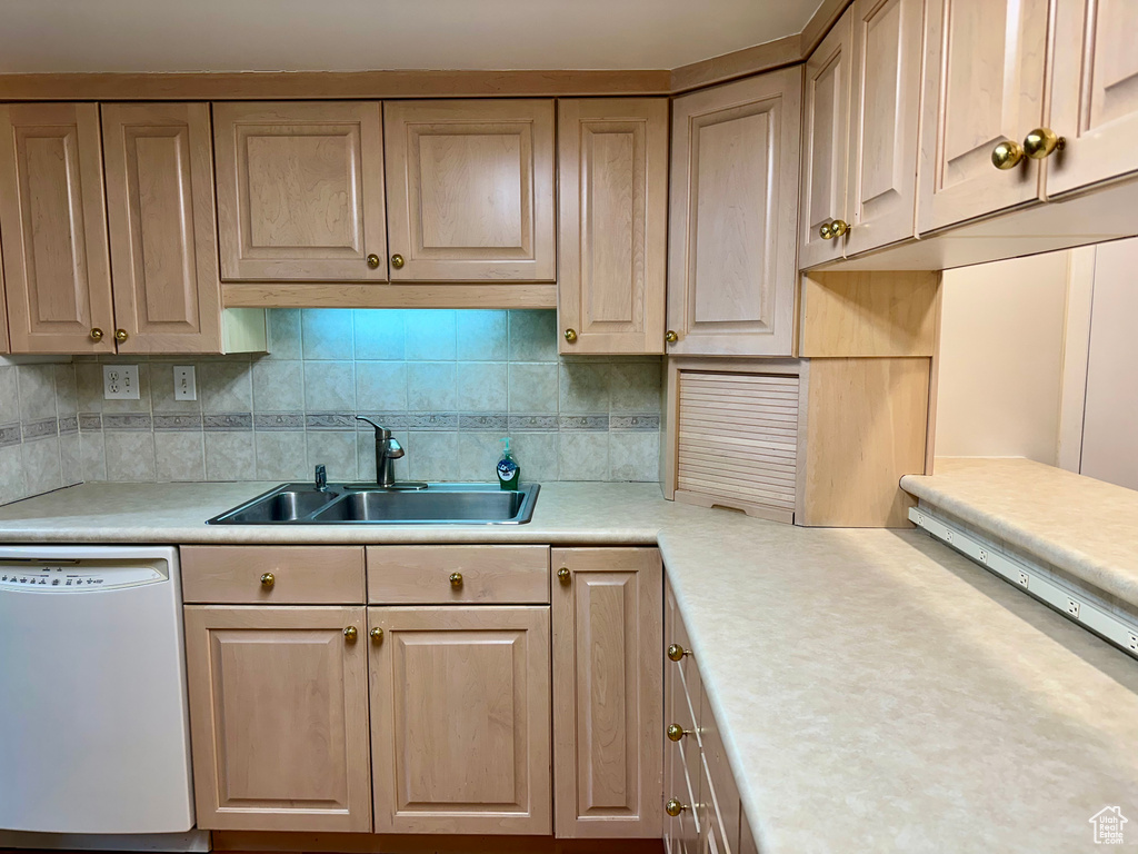 Kitchen with backsplash, white dishwasher, sink, and light brown cabinets