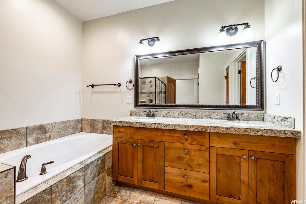 Bathroom featuring mirror, a relaxing tiled bath, double sink vanity, and light tile floors