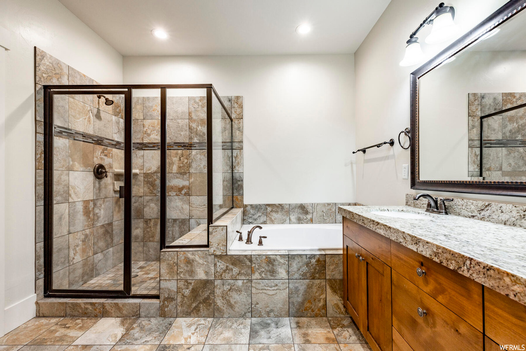 Bathroom featuring mirror, light tile flooring, vanity, and shower with separate bathtub