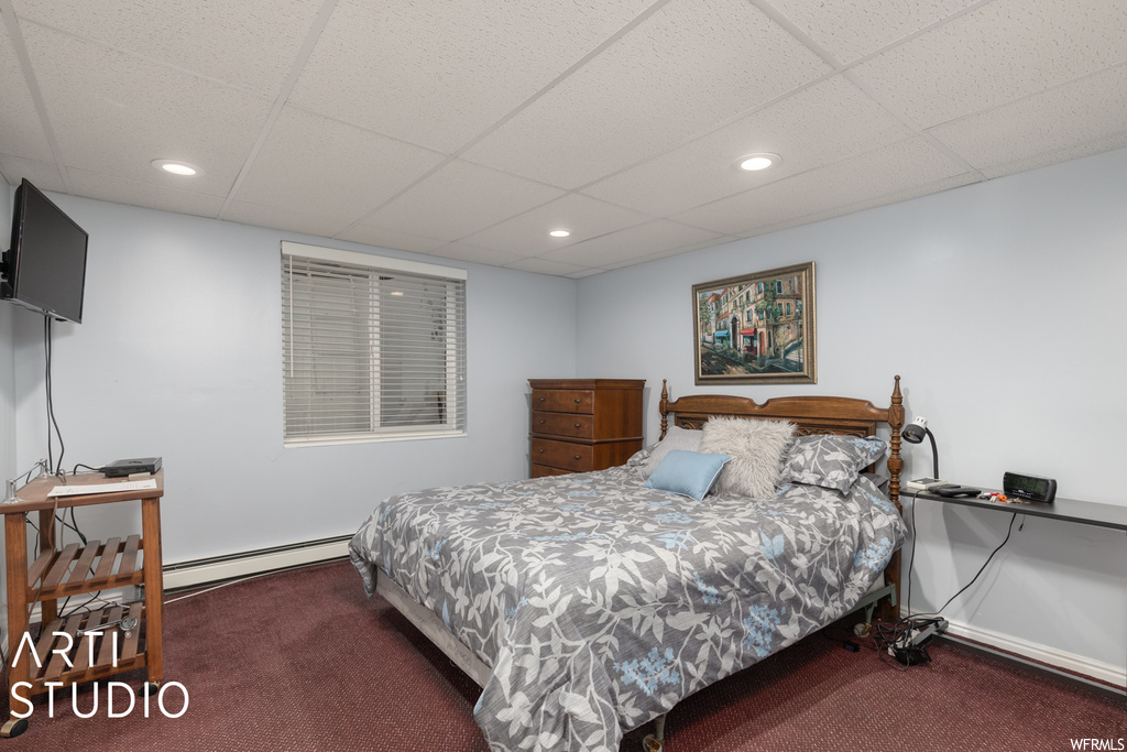 Bedroom featuring dark carpet, a baseboard heating unit, and a drop ceiling