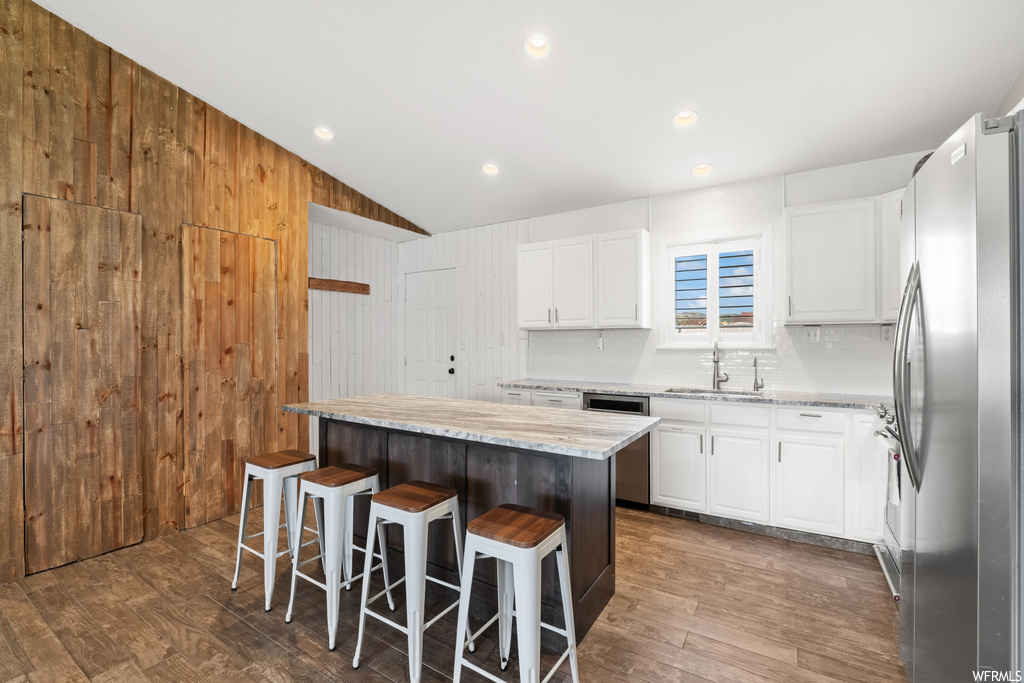 Kitchen featuring stainless steel fridge, wood walls, lofted ceiling, backsplash, white cabinetry, hardwood flooring, and a center island