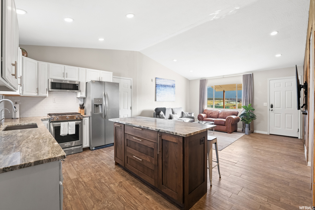 Kitchen with light hardwood flooring, stainless steel appliances, lofted ceiling, backsplash, and light stone countertops