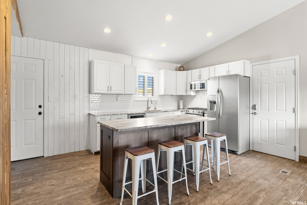 Kitchen with stainless steel appliances, white cabinets, light countertops, backsplash, vaulted ceiling, light hardwood floors, and a center island