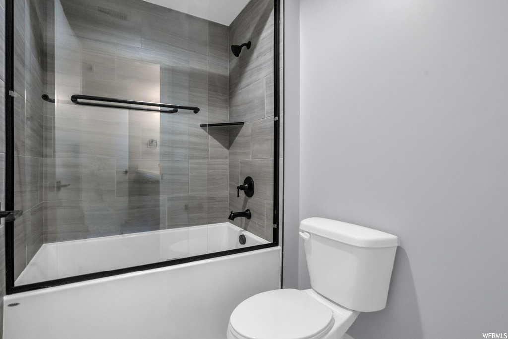 Bathroom featuring toilet and shower / bath combination with glass door