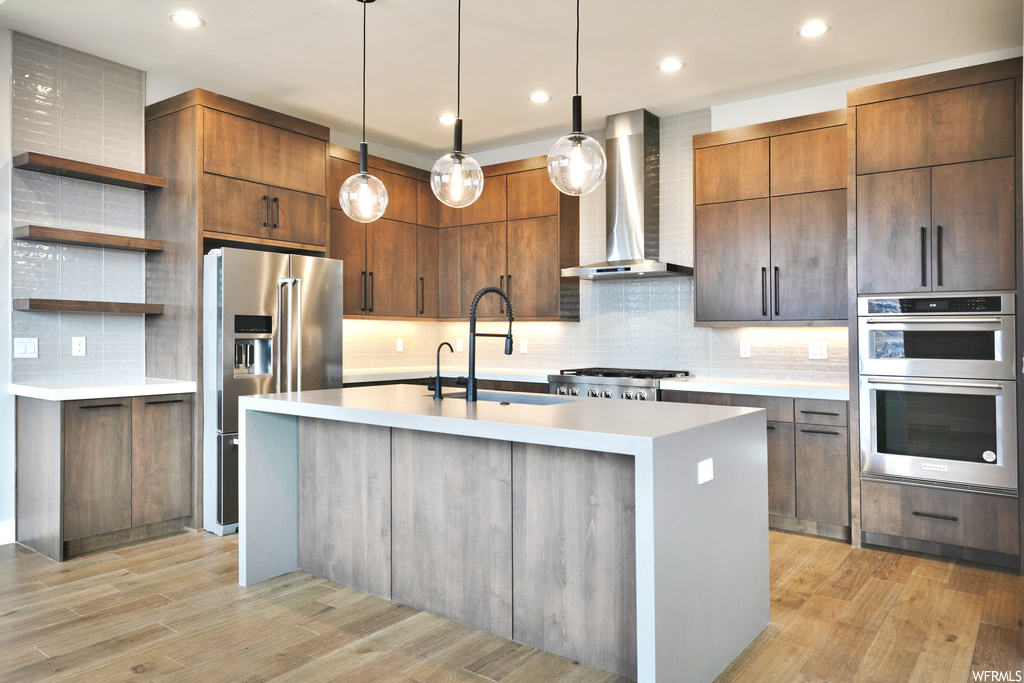 Kitchen featuring wall chimney range hood, light hardwood / wood-style floors, tasteful backsplash, and appliances with stainless steel finishes