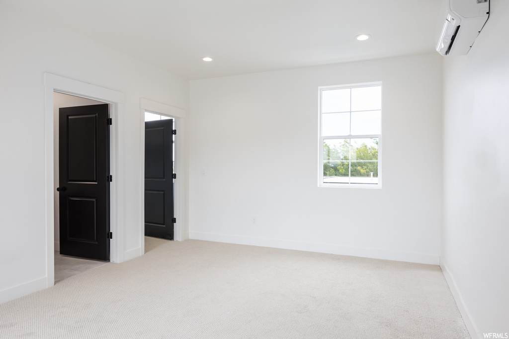 Unfurnished room with light carpet and a wall unit AC