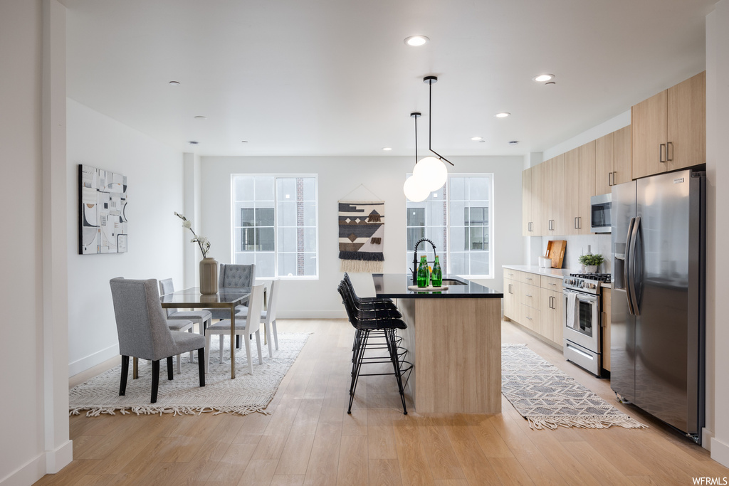 Kitchen featuring light hardwood flooring, pendant lighting, dark countertops, a center island, and appliances with stainless steel finishes