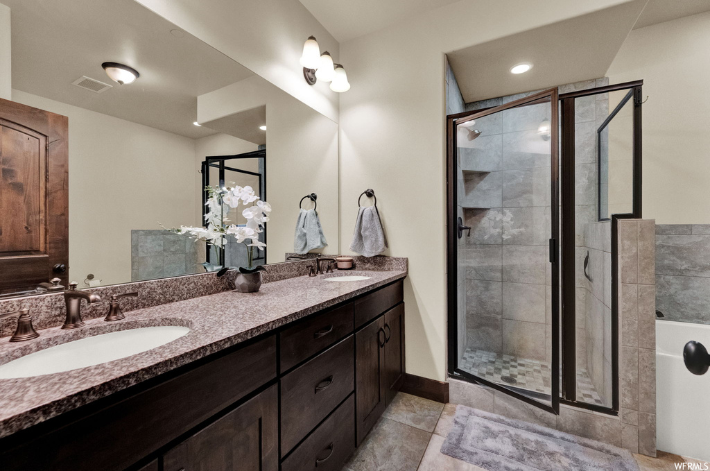 Bathroom with light tile floors, a shower with door, mirror, and double large sink vanity