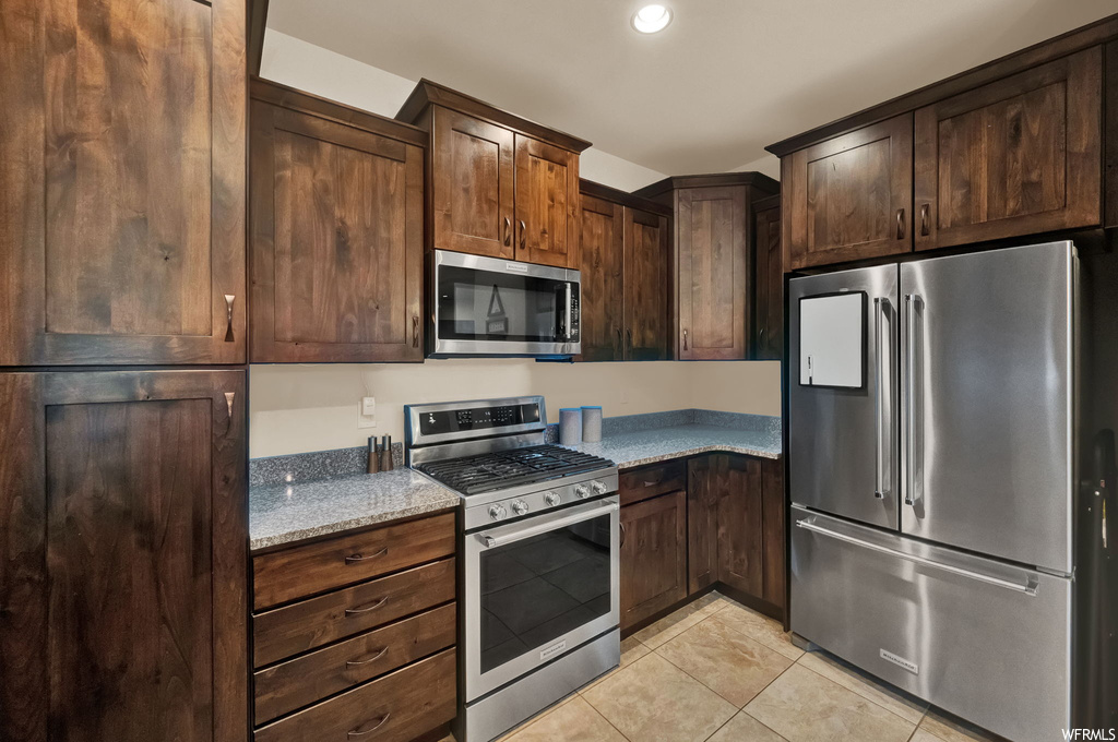 Kitchen with dark brown cabinets, light tile flooring, and appliances with stainless steel finishes