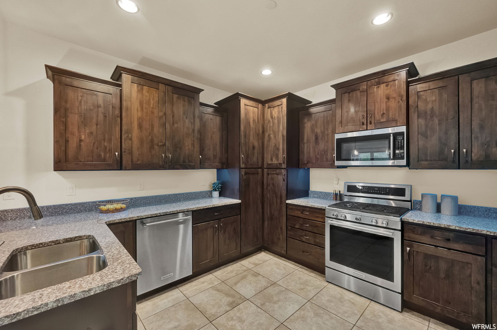 Kitchen with dark brown cabinets, light stone counters, stainless steel appliances, and light tile floors
