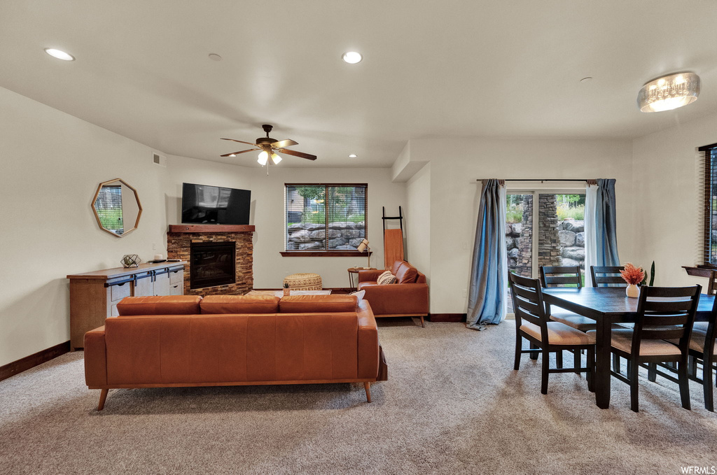 Living room featuring ceiling fan, a fireplace, light carpet, and plenty of natural light