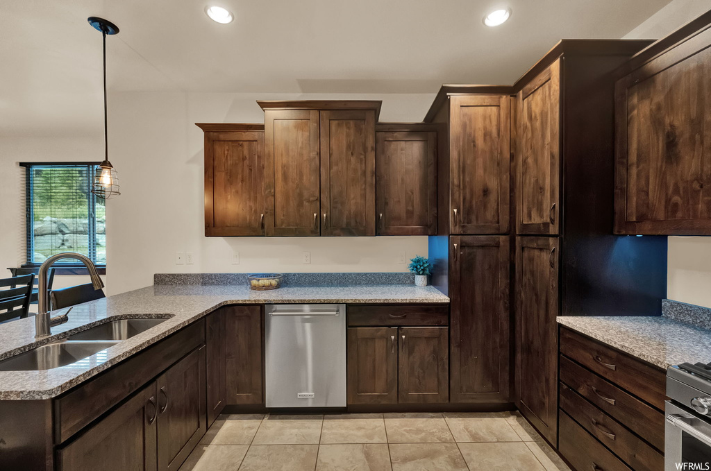 Kitchen featuring light tile floors, dark brown cabinets, light granite-like countertops, decorative light fixtures, and stainless steel dishwasher