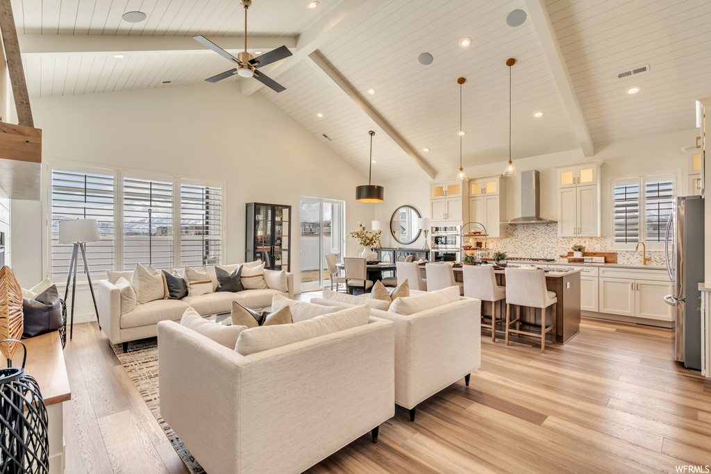 Living room featuring wooden ceiling, light hardwood flooring, a wealth of natural light, a high ceiling, ceiling fan, and lofted ceiling with beams