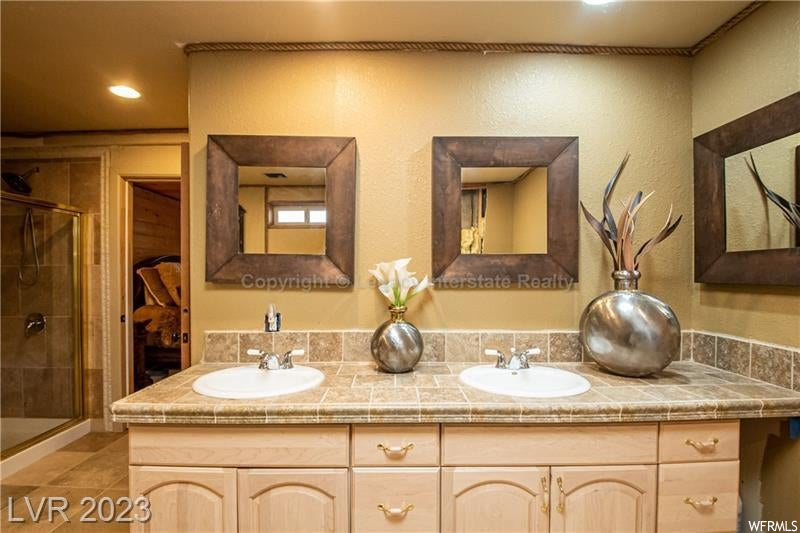 Bathroom featuring double sink vanity, mirror, a shower with shower door, and tile flooring