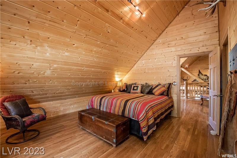 Bedroom with lofted ceiling, light hardwood floors, wooden walls, and wood ceiling