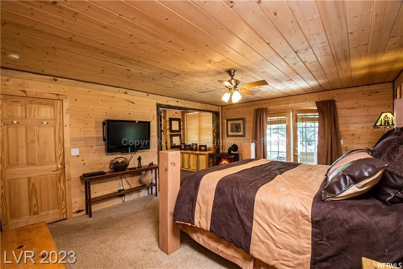 Carpeted bedroom with wood walls, ceiling fan, and wooden ceiling