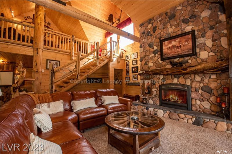 Carpeted living room with wood ceiling, log walls, a high ceiling, lofted ceiling with beams, and a fireplace